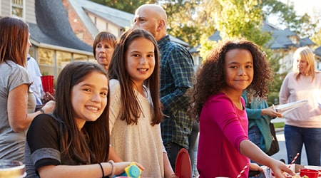 A group of people enjoys a neighborhood block party, with smiling children in the front and adults mingling in the background