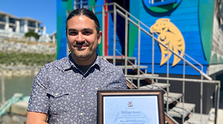 Anthony Meza Wilson posing with award in front of the Blue Cabin