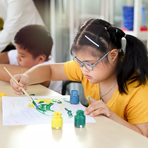 A girl with a disability painting in an art class