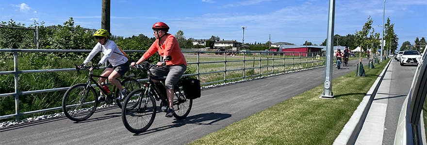 Three people riding bicycles on a trail near the river