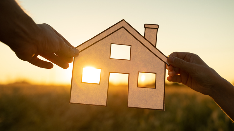 Two hands  holding a paper home in sunset