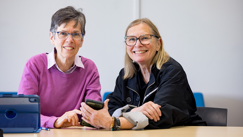 Two seniors sitting at a table with an ipad and phone