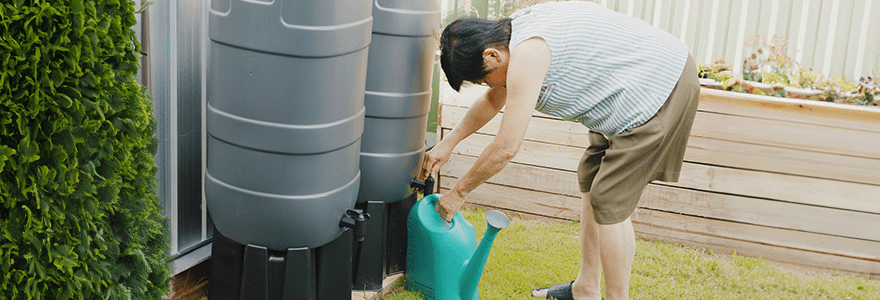 Woman filling a watering can with the water in a rain barrel