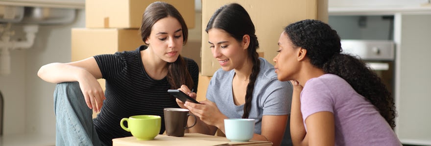View of three young females looking at a mobile phone amongst moving boxes