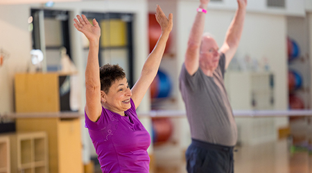 Two older adults participating in a fitness class in an indoor gym setting