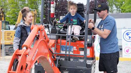 A little girl testing out the digger at Public Works Open house, supported by event volunteers