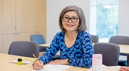 Asian woman sitting at a desk doing a pencil sketch.