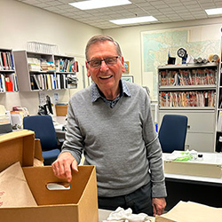A smiling man with a box of papers in an archive room