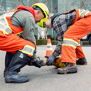 Two utility workers lifting a heavy hose on a street during maintenance work