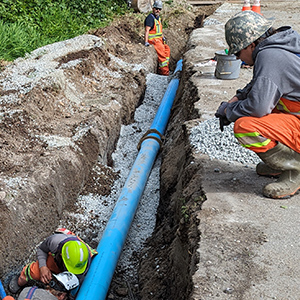 Construction crew installing a large water pipe in a trench alongside a road