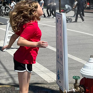Girl cooling off at a sidewalk misting station on a sunny day